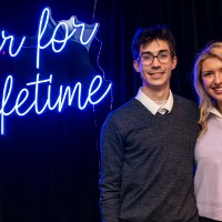 Girl and boy pose together in front of Laker for a Lifetime neon sign.